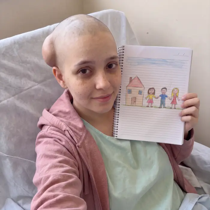 Ela segurando um caderno com o desenho de uma casa e uma família